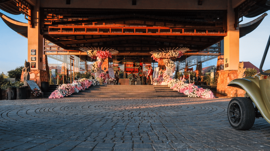 The main entrance of Ananta Spa & Resort, Jaipur, is adorned with garlands of pink and white flowers along the paved driveway.