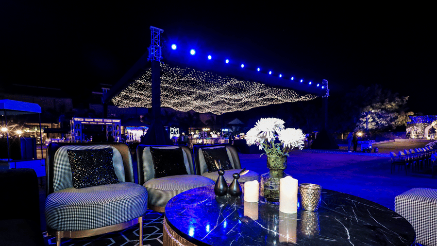 Outdoor lounge setup with round tables and chairs under blue lights at Ananta Spa and Resorts, Jaipur.