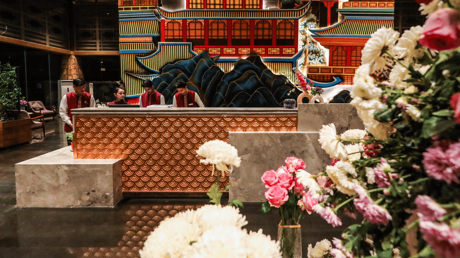 Large white and pink floral arrangements stand near the reception desk at Ananta Spa & Resort, Jaipur, with the pagoda mural visible.