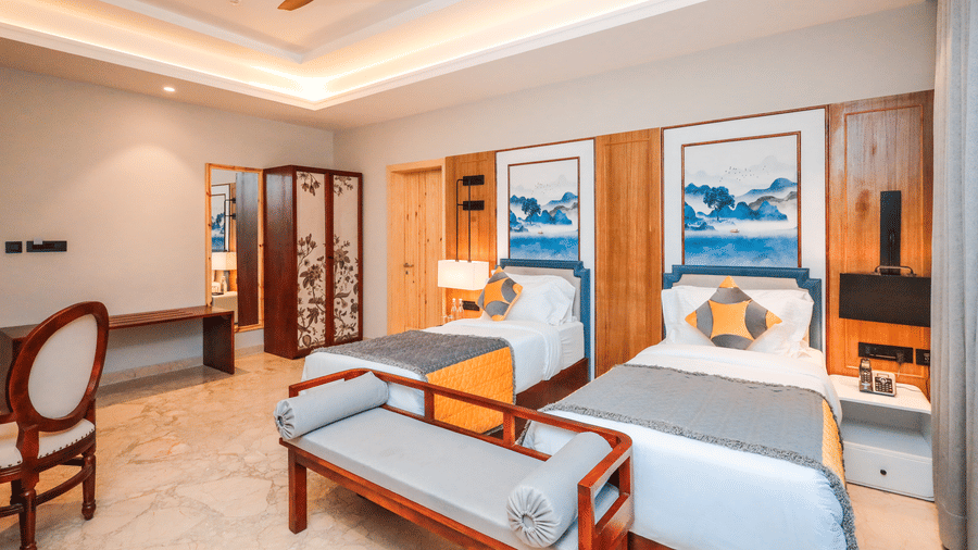 A room shows a bed with side tables, chairs with a table, storage units, artwork on the wall and a doorway at Ananta Spa & Resort, Jaipur.