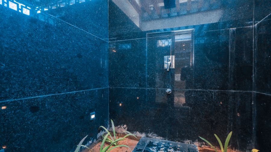 An outdoor space shows a high tiled wall with flowing water falling into a planted area at Ananta Spa & Resort, Jaipur.