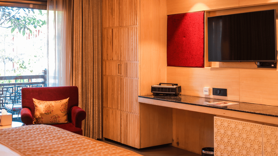 A room with a bed, seating, a desk, mounted television and storage unit at Ananta Spa & Resort, Jaipur.