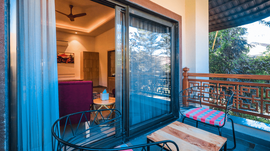 A balcony with chairs, a table, and a sliding door leading to an indoor room at Ananta Spa & Resort, Jaipur.
