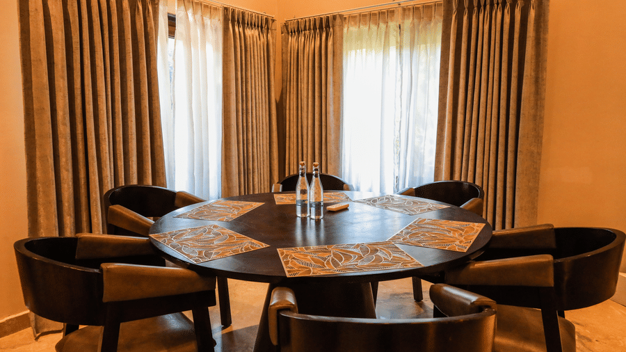 A room shows a round dining table with chairs placed around it near a window with long curtains at Ananta Spa & Resort, Jaipur.