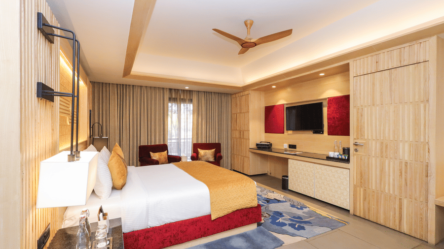 An overview of a bedroom in Jaipur at Ananta Spa & Resort., Jaipur, with a king size bed, ceiling fan, side tables and a TV.