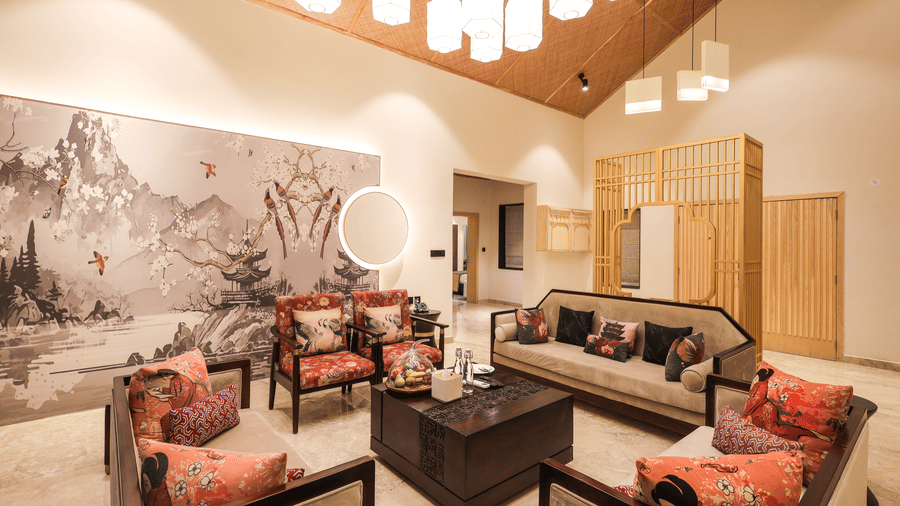 A room shows a sofa set with a centre table, chairs on both sides, a wall artwork behind the seating and cabinets to one side at Ananta Spa & Resort, Jaipur.