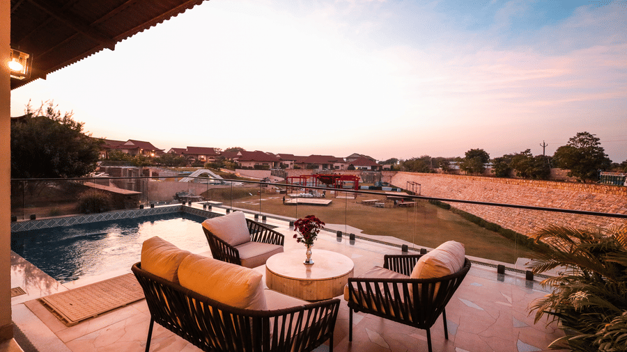 Outdoor space shows lounge chairs and tables beside a pool with landscape views in the distance at Ananta Spa & Resort, Jaipur.