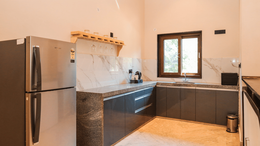 A fully equipped kitchen shows a refrigerator, a counter with cabinets, a sink, a stove and a window above the workspace at the Presidential Suite of Ananta Spa & Resort, Jaipur.