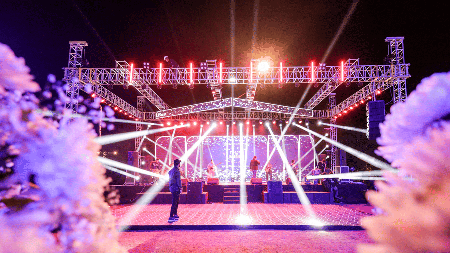 A large, brightly lit performance stage at Ananta Spa & Resort, Jaipur, is surrounded by white floral decorations in the foreground.
