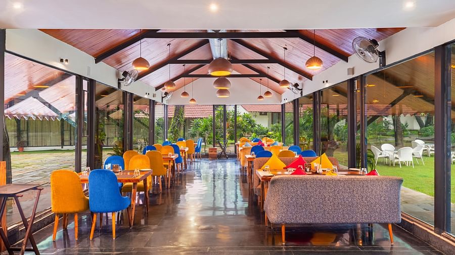 an image of the kalptaru multi-cuisine restaurant with yellow and blue cushioned chairs with an empty alley in the middle at aranya vilas in udaipur
