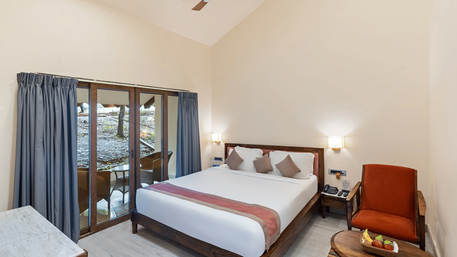 Bedroom of a Luxury Family Suite at Aranya Vilas by Mertia Hospitality featuring a plush bed, wooden furnishings, seating area, and glass doors opening to a private balcony.