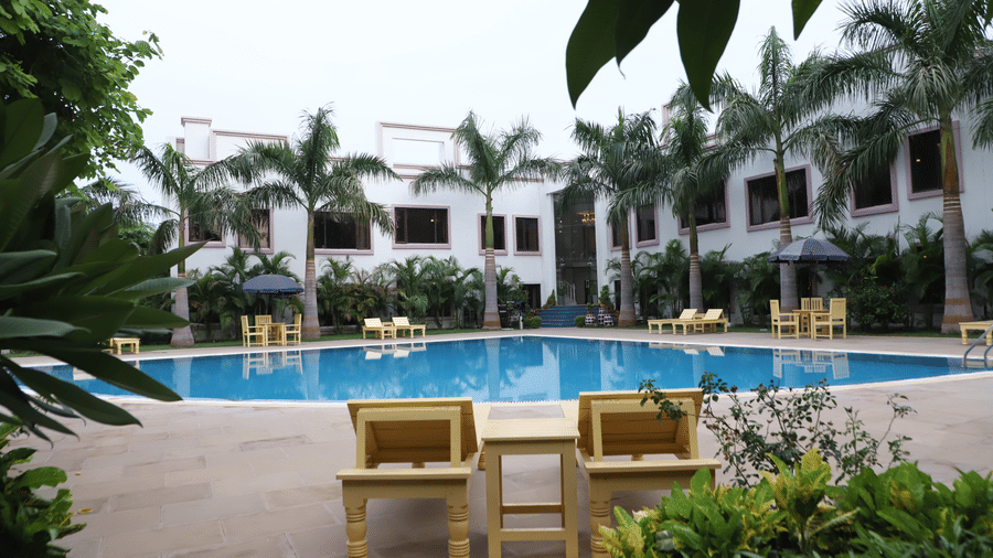 A swimming pool with chairs and palm trees at AS Hotels, Khajuraho.