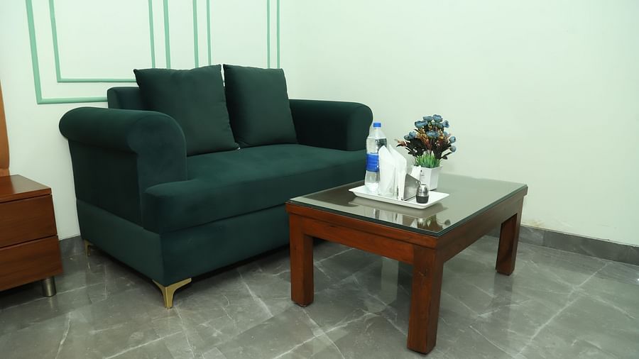 A seating area with a dark green sofa, cushions, and a small coffee table on a tiled floor - Asian Suites IFFCO Metro, Gurgaon