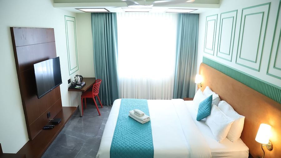 A bright room featuring a double bed with a blue runner, bedside tables, and a television - Asian Suites IFFCO Metro, Gurgaon