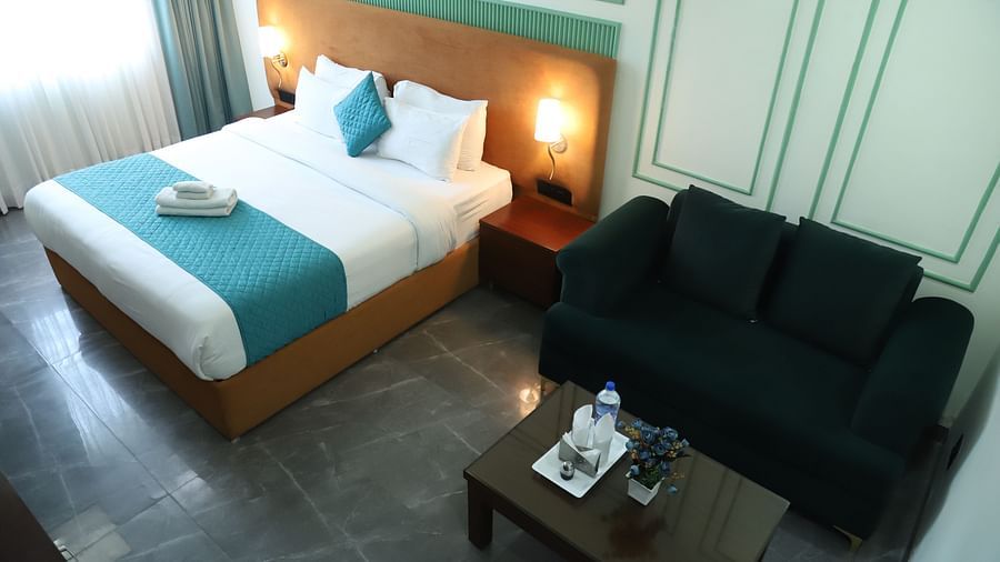 A room with a double bed featuring a blue and white design, alongside a dark coloured sofa - Asian Suites IFFCO Metro, Gurgaon