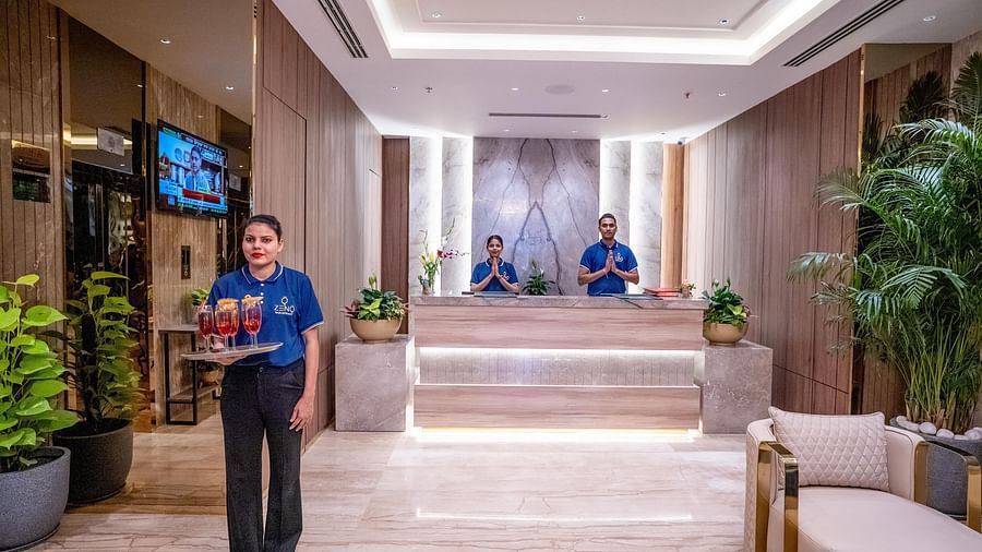 Reception desk with modern design, lighting, plants and staff member standing with drinks in her hand at ASTER GRAND BY ZENQ SAKET.