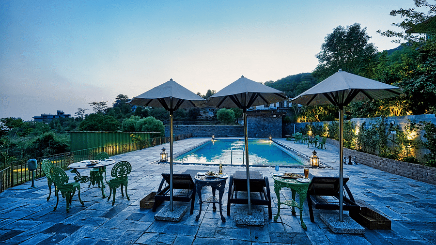 An image of outdoor pool with lounge chairs and umbrellas, surrounded by greenery - Atman, Dharamshala.