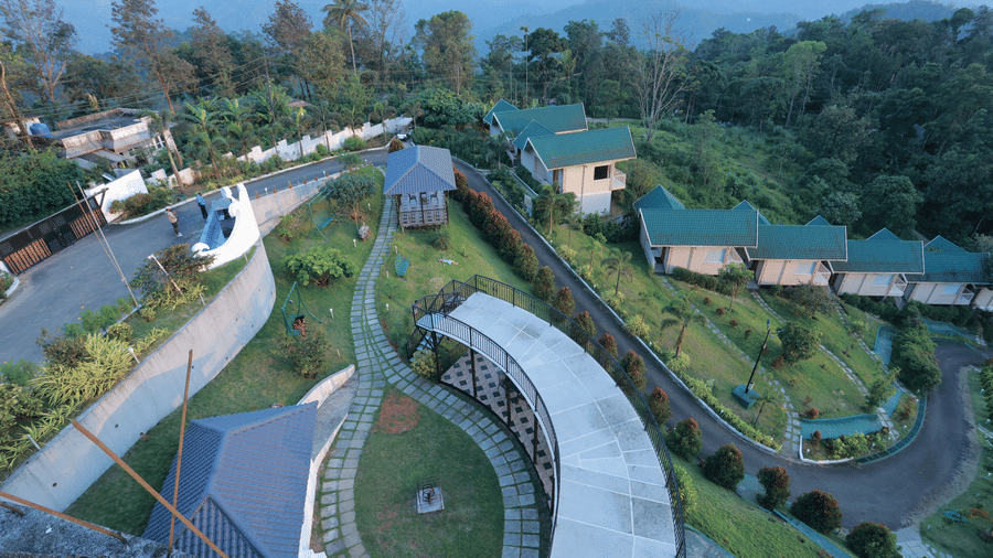 A bird's eye view of the Aveda Mountains and Mist Resort and Spa, Munnar, showcasing several villas surrounded by green lawns.