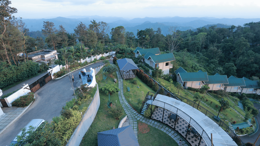 A bird's eye view of the Aveda Mountains and Mist Resort and Spa, Munnar, with beautiful mountain valleys covered in mist merging with the horizon.