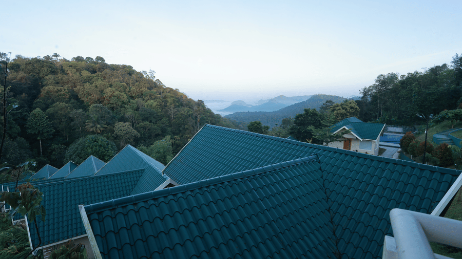A panoramic shot of the misty mountain valleys with the bricked turquoise roof of the villas at Aveda Mountains and Mist Resort and Spa, Munnar, in the foreground.