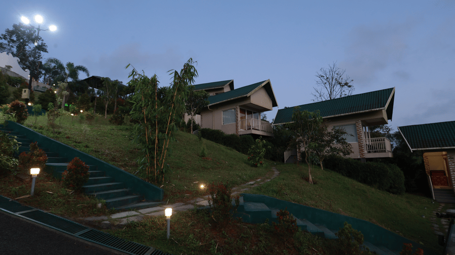 A green lawn sloping downhill with several exterior lights illuminating the exterior at Aveda Mountains and Mist Resort and Spa, Munnar.