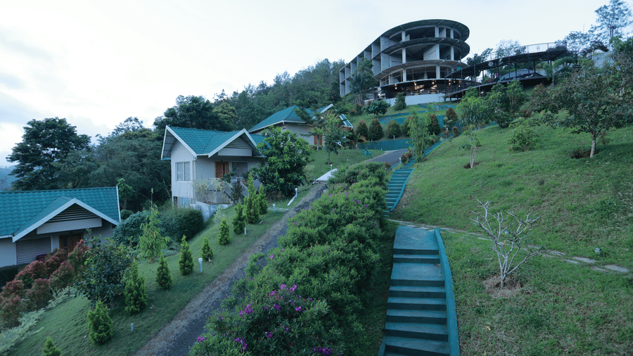 A wide-angle shot featuring the lush green lawns at Aveda Mountains and Mist Resort and Spa, Munnar, with several villas scattered.