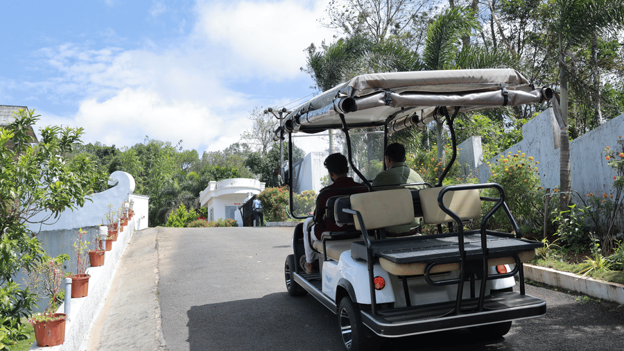 A golf cart with 2 people sitting in the front seat driving on a road at Aveda Mountains and Mist Resort and Spa, Munnar.