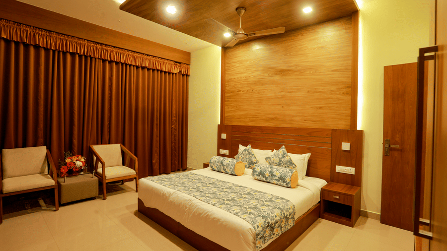 A plush double bed at Luxe Mountain View 2-Bedroom Family Villa along with 2 arm chairs placed in front of the windows covered with brown blackout curtains at Aveda Mountains and Mist Resort and Spa, Munnar.
