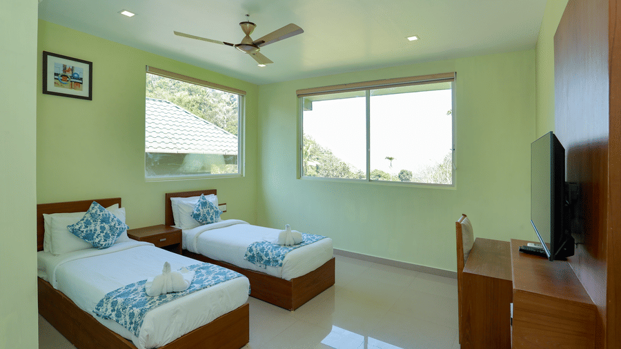 A bedroom with ample of natural light featuring a set of twin beds with a ceiling fan at Luxe Mountain View 2-Bedroom Family Villa of Aveda Mountains and Mist Resort and Spa, Munnar.