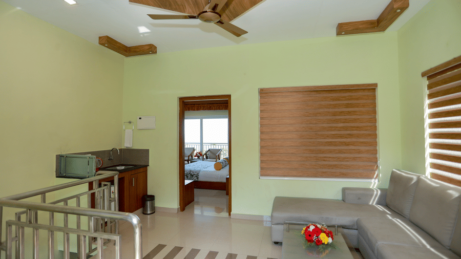 Living area with L-shaped sofa, coffee table, stair railing, and small kitchenette setup.