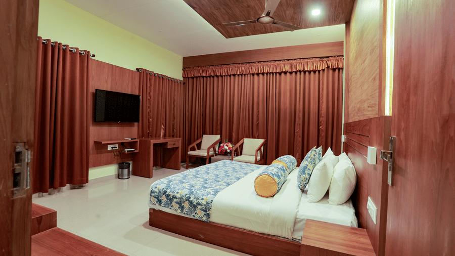 Bedroom with wooden double bed, bolster pillow, wall-mounted TV, and full-height red drapes.