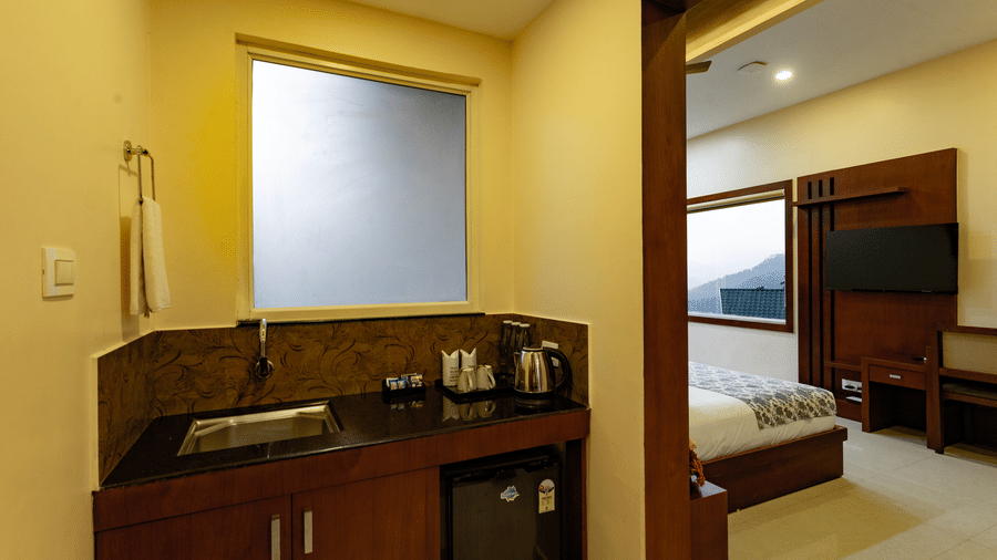A vanity area with a mini fridge below the slab alongside a doorway opening to the bedroom of Luxe Mountain View Cottage at Aveda Mountains and Mist Resort and Spa, Munnar.