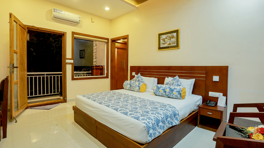 Corner view of the Luxe Mountain View Cottage featuring a double bed with a bed side table, and a door opening to the balcony during night time at Aveda Mountains and Mist Resort and Spa, Munnar.