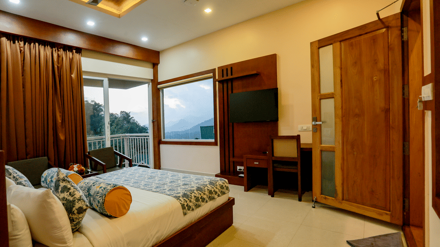 A wide-angle shot of the Luxe Mountain View Cottage at Aveda Mountains and Mist Resort and Spa, Munnar, featuring a double bed with a lot of pillows and cushions facing the wall-mounted television.