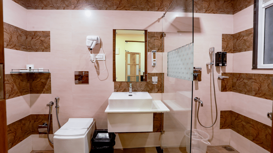 The bathroom at the Luxe Mountain View Cottage at Aveda Mountains and Mist Resort and Spa, Munnar, featuring a shower area, a commode, and a wash basin.