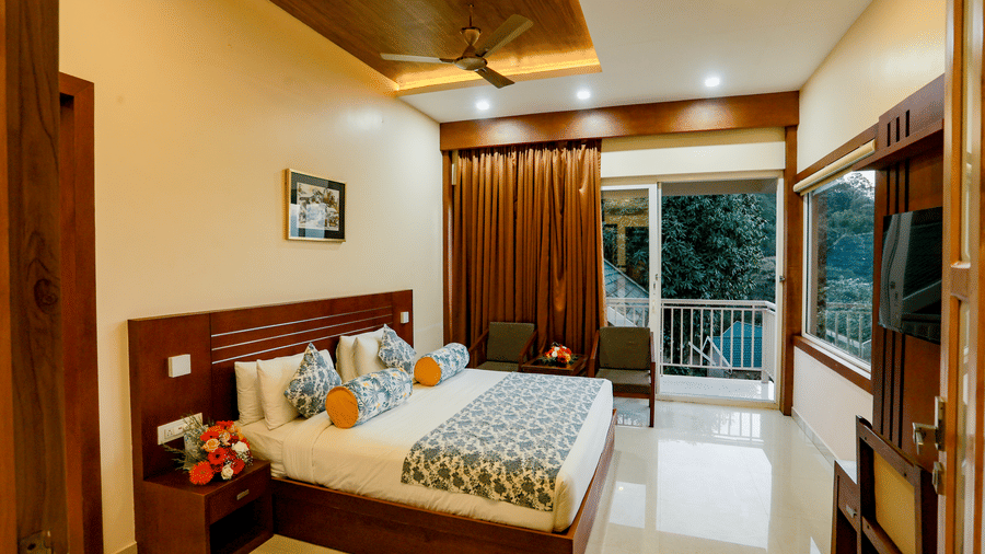 Full view of thr Luxe Mountain View Cottage featuring a double bed and lush green views of the mountain valley from the balcony at Aveda Mountains and Mist Resort and Spa, Munnar.
