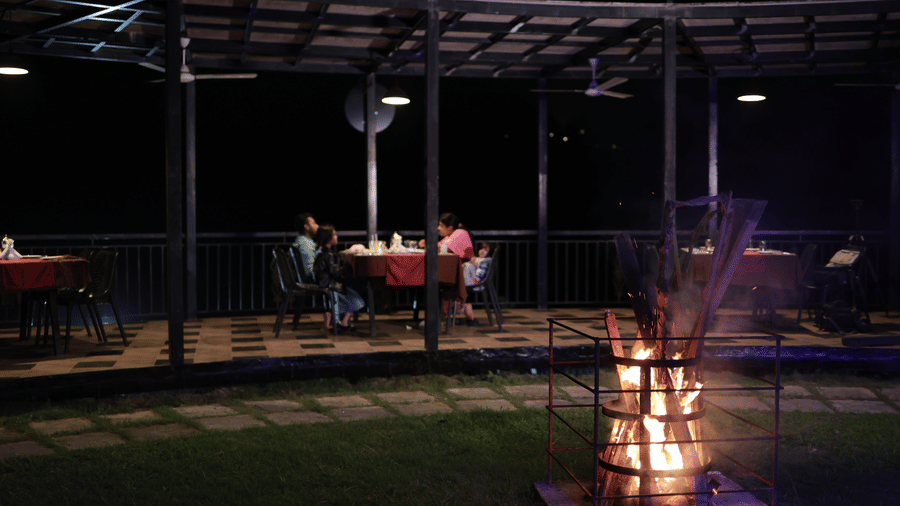 The bonfire pit buring in the middle of the lawn along with the dining area of the Machaan restaurant in the background at Aveda Mountains and Mist Resort and Spa, Munnar.