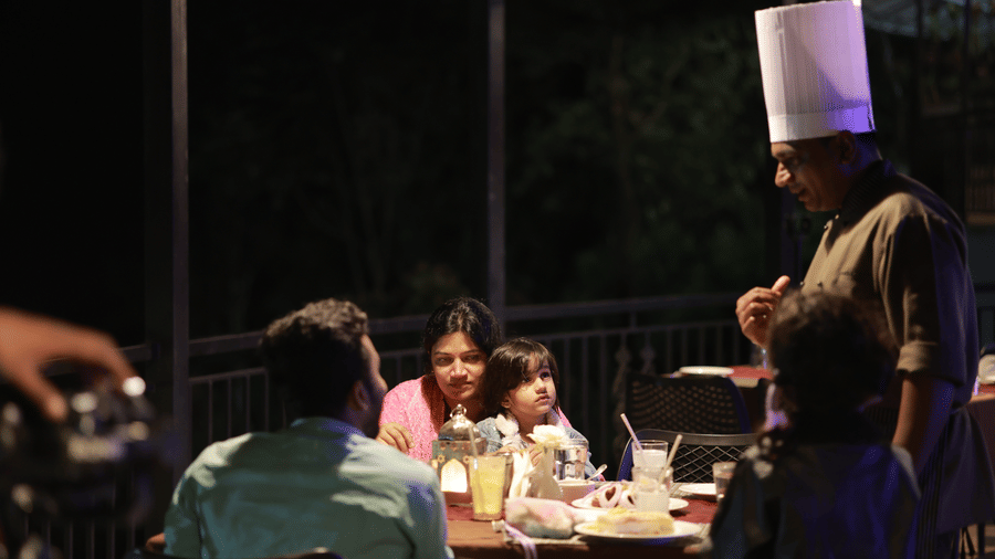 A person wearing the chef's hat having a conversation with a man seated with his family at the Machaan restaurant at Aveda Mountains and Mist Resort and Spa, Munnar.