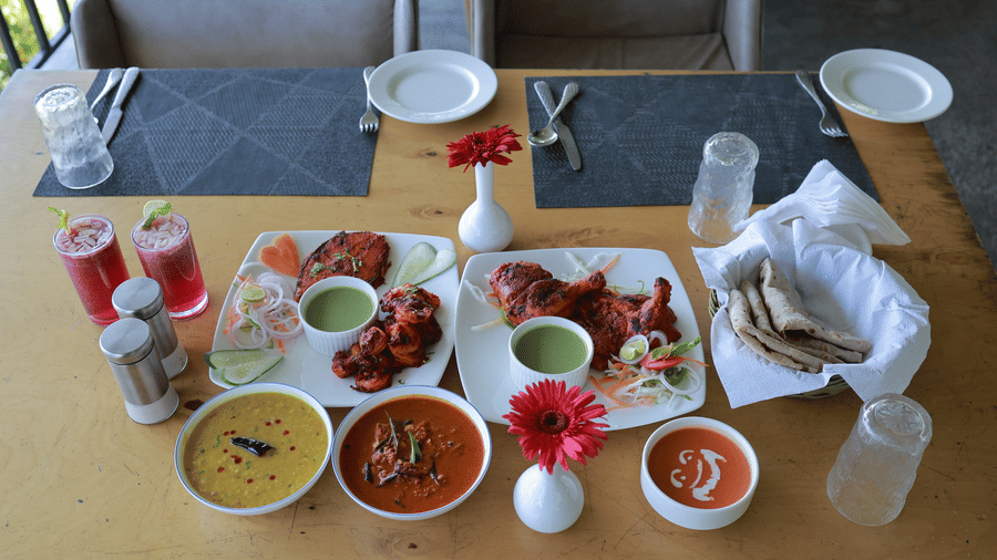 Full view of the entire Indian meal served along with mocktails on a dining table of the Machaan restaurant at Aveda Mountains and Mist Resort and Spa, Munnar.