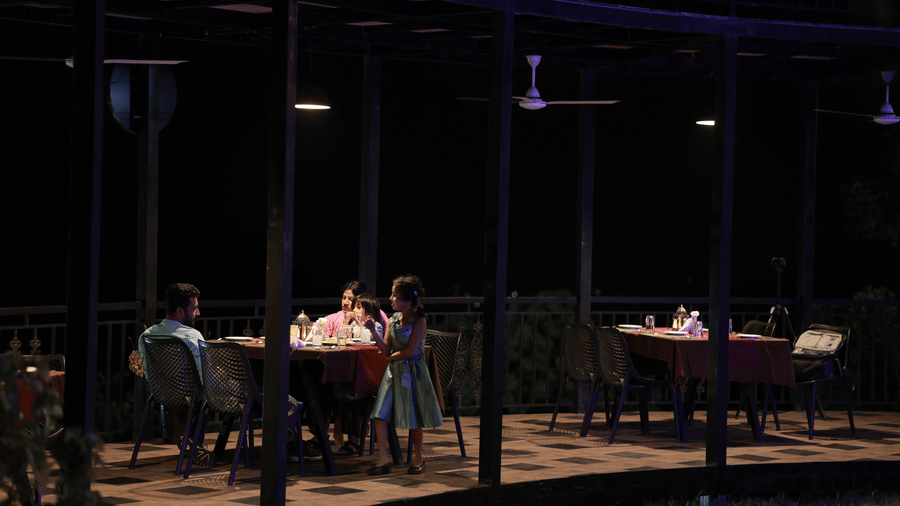 Full view of the outdoor dining area of the Machaan restaurant during the night featruing a family of 3 at Aveda Mountains and Mist Resort and Spa, Munnar.