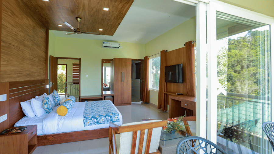 Wide view of spacious suite bedroom with king bed, wooden interior panels, TV console, and desk.