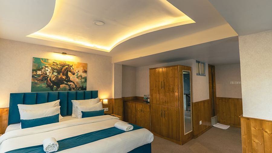 Deluxe Room with a king size bed, inviting ambiance, wooden bedside table, and wooden cupboard at Avianna Seven Seas, Darjeeling.