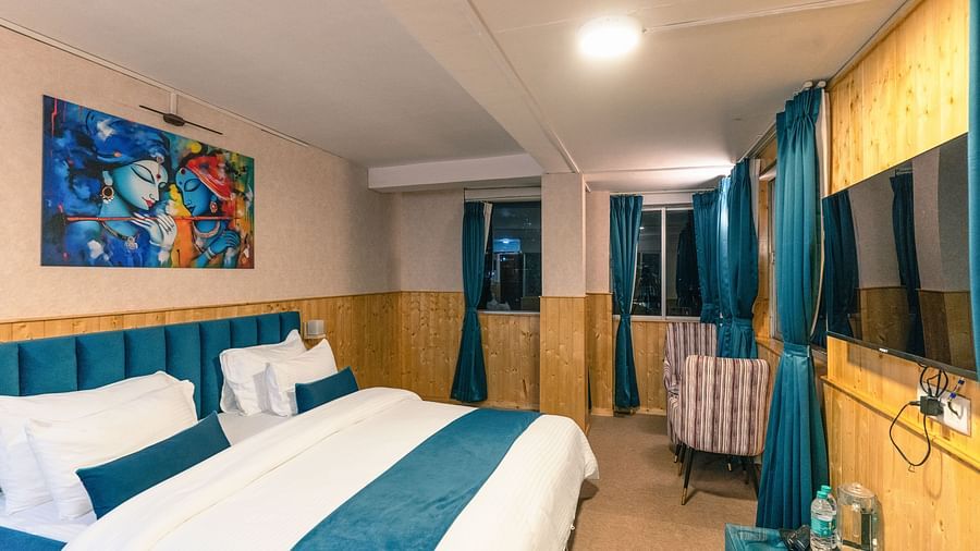 Deluxe Room with a king size bed, inviting ambiance, wooden bedside table, and a wall mounted television at Avianna Seven Seas, Darjeeling.
