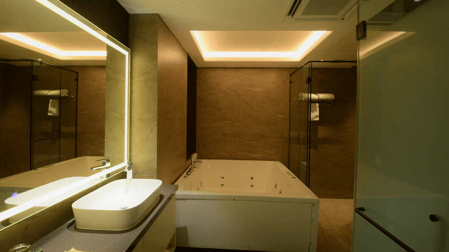 A bathroom interior featuring a large white bathtub, a modern washbasin with a backlit mirror, and a shower stall at Awesome Palace, Guwahati Airport.