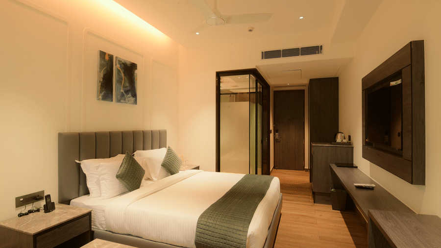 A hotel bedroom featuring a neat king size bed, a wall-mounted television, a large wardrobe, and a glass door at Awesome Palace, Guwahati Airport.