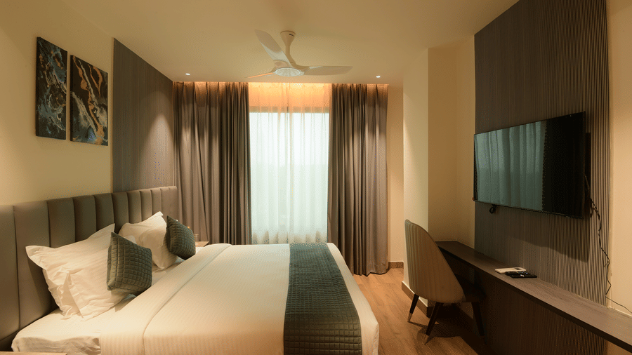 A king size bed facing a wall mounted television, a desk, and curtains at Awesome Palace, Guwahati Airport.