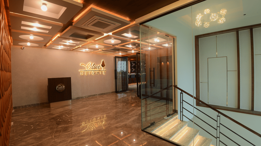 A well-lit hotel reception lobby area with a marble floor, a glass panelled staircase railing, and a reception desk at Awesome Palace, Guwahati Airport.