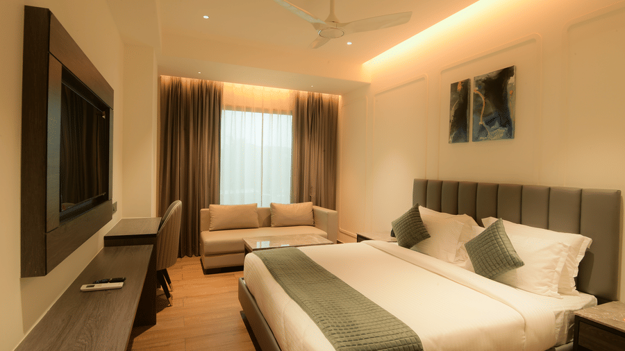 A spacious room with a comfortable king size bed, a television, a sofa near the window, and a study desk at Awesome Palace, Guwahati Airport.