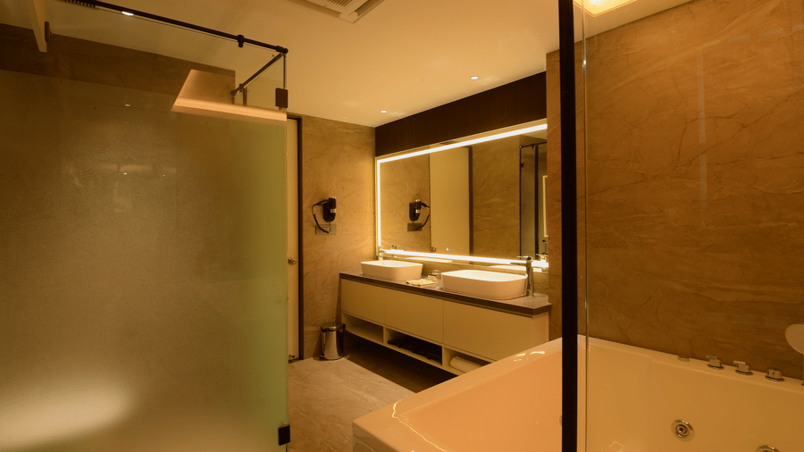 A bathroom equipped with a double vanity sink unit, a large illuminated wall mirror, and a corner bathtub at Awesome Palace, Guwahati Airport.