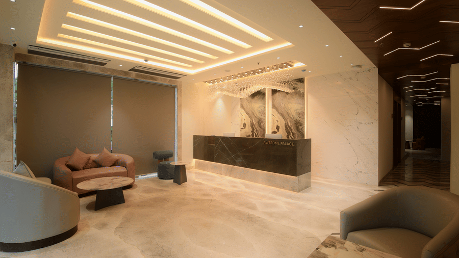 A reception area with a marble front desk, comfortable seating arrangements, and elegant lighting on the ceiling at Awesome Palace, Guwahati Airport.